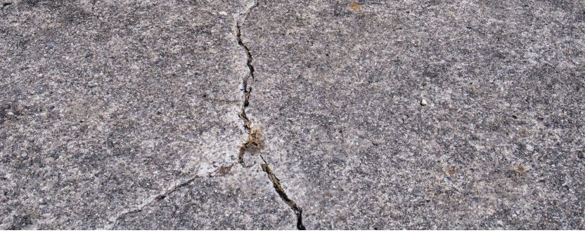 A close-up view of a cracked concrete surface, showing a jagged line running through the rough, gray texture—typical wear that a residential concrete company can expertly repair.
