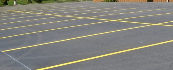 Empty parking lot with freshly painted yellow lines marking parking spaces on a smooth asphalt surface, part of a building visible in the background—ideal for those seeking quality concrete driveway repair from a trusted concrete company in Tampa.