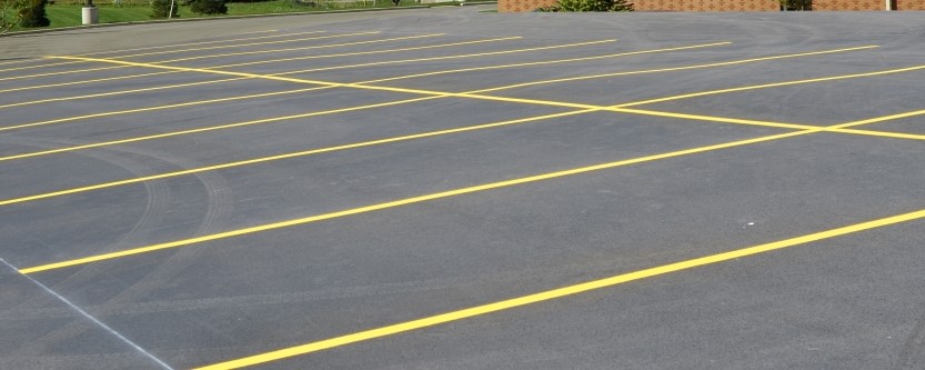 Empty parking lot with freshly painted yellow lines marking parking spaces on a smooth asphalt surface, part of a building visible in the background—ideal for those seeking quality concrete driveway repair from a trusted concrete company in Tampa.