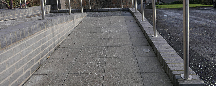 A concrete wheelchair-accessible ramp with metal handrails on both sides, bordered by brick walls, demonstrates expert concrete service while leading up to a building entrance.