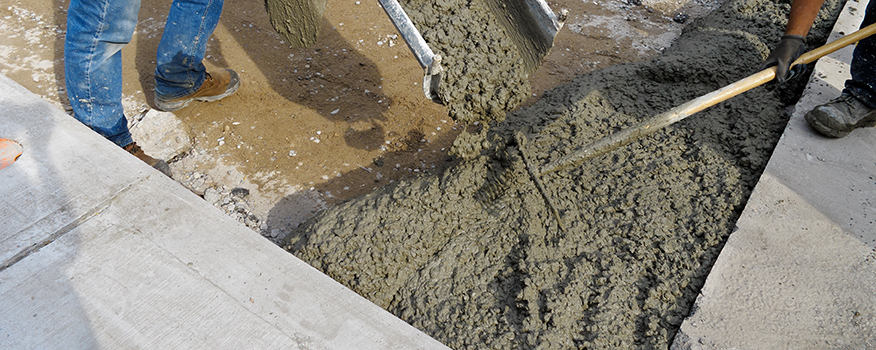 Fresh concrete is being poured from a chute into a prepared area, while two workers use tools to spread and level the mix—a typical day for a top concrete company Tampa relies on for quality concrete service.