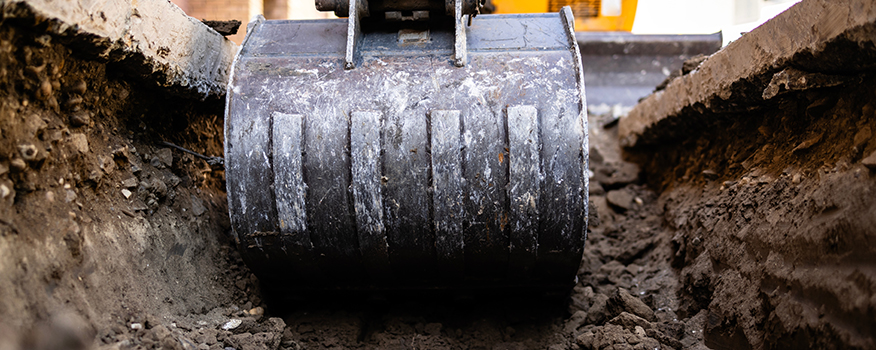 Close-up view of an excavator bucket digging into the ground, surrounded by soil, captured during a construction project for a residential concrete company.