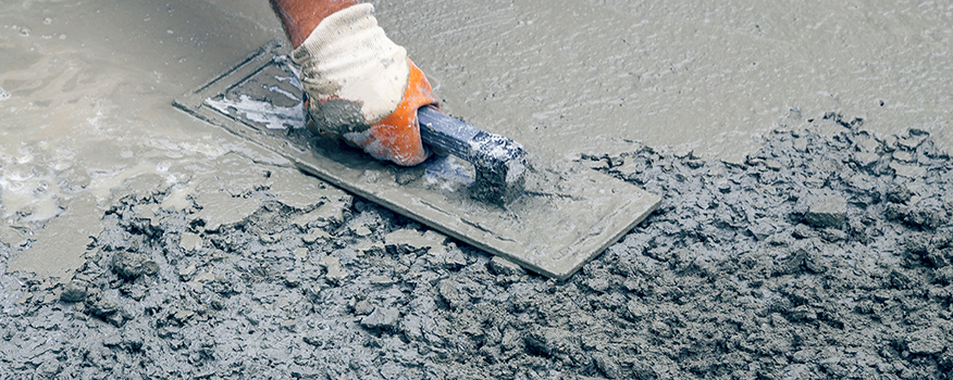 A gloved hand smooths wet concrete with a trowel, leveling the surface during concrete driveway repair by a residential concrete company.