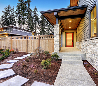 Modern house with stone accents, a covered front porch, and a red door. Concrete steps, expertly crafted by a concrete company Tampa trusts, lead through a landscaped front yard with mulch, small plants, and a wooden privacy fence.
