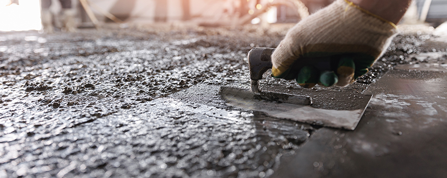 A gloved hand smooths wet concrete with a trowel, leveling the surface during a construction project—a testament to the precision and skill of a top residential concrete company. The focus is on the hand and the tool in action.