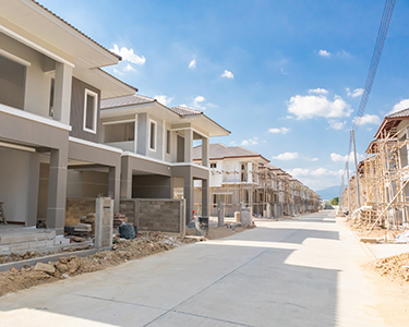 A wide street lined with newly constructed, modern two-story houses under a bright blue sky; some homes showcase fresh driveways thanks to expert residential concrete company services, while others are still under construction.