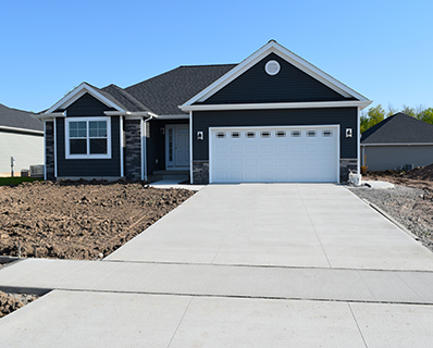 A newly built, dark blue single-story house with a white garage door and a wide concrete driveway installed by a trusted residential concrete company. The yard is bare dirt, indicating recent construction and no landscaping yet.